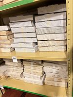 Shelf holding multiple stacks of white striped and plain cardboard plate boxes