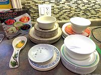 Lot overview showing stacked plates, bowls, boxed Paderno dip set