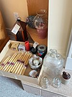 Mixed décor items arranged; shows lantern, glass hurricane with pillar candle, apothecary jar, beeswax candles, insulators, crock, shell holder and more