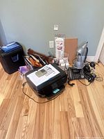 Group view of printer, shredder, lamp, telephone, file organizer, binder, thermometer, pen cup and cables on floor