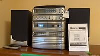 Front view of Memorex 9198M stereo flanked by two speakers; remote and manual also visible