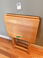 Two wooden folding TV tables nested upright against wall