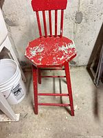 Front view of red wooden stool showing octagonal seat, spindle back, legs and distressed paint
