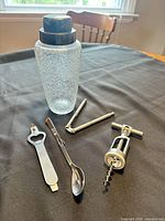 crackle glass shaker, nutcracker, corkscrew, bottle opener, mixing spoon displayed on table
