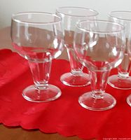Four clear stemmed beer glasses on red cloth