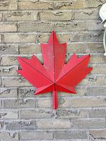 Front view of red aluminum maple leaf wall décor mounted on brick wall
