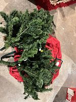 Sectional branches of green artificial tree with integrated lights atop red storage bag