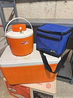 All three items: orange Coleman chest cooler, orange Coleman PolyLite jug, blue Arctic Zone soft cooler