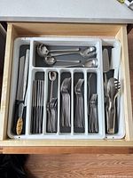 Drawer view with white organizer holding assorted flatware and kitchen knives