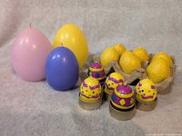 Group view of all egg-themed candles: three pastel pillar candles, six yellow votives in tray, five decorated tea lights