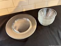 Stack of six clear glass bowls beside stack of four clear glass plates