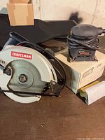 Craftsman circular saw beside Black & Decker palm sander on table