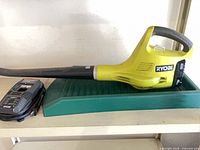 Ryobi leaf blower with battery attached and charger beside it on shelf