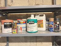 Shelf with two BEHR paint cans, Varsol jug, three spray paint cans, several filler tubs