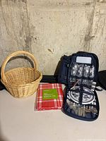 Overall lot showing wicker basket, sealed tablecloth and opened picnic backpack with contents