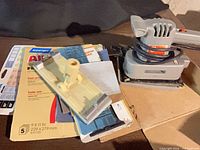 Lot showing Black & Decker finishing sander, drywall hand-sander block and Norton sandpaper sheets