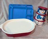 Group view of red oval server with lid, blue divided tray, stacked snowman canisters