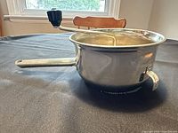 side view of stainless steel food mill showing handle, crank knob and pot-rest hook