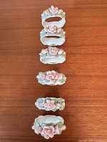 Six porcelain napkin rings arranged vertically on wooden surface, showing floral decoration