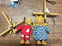 Both wooden boy and girl marionette puppets with controllers visible, strings tangled