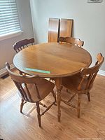Round wooden table with four chairs and two leaves against wall