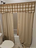 Beige curtain panels with checked valance installed on bathtub