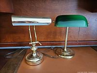 Both brass banker lamps side by side on desk