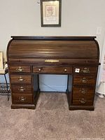 Front view of dark brown wood roll-top desk with drawers and brass hardware