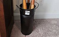 Full view of cylindrical black metal umbrella stand with side handles, contents inside for scale