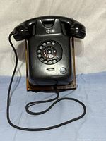 Front view showing Bakelite body, rotary dial, handset, cord and wood backboard
