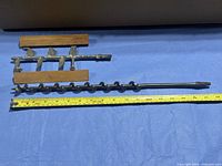 auger drill bit and butter churn paddle laid beside tape for scale