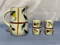 Front view of pitcher and two cups showing fruit motif