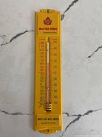 Front view of yellow MLM Master Feeds thermometer showing full scale and logo