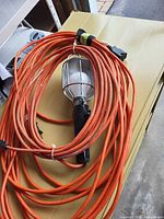Coiled orange extension cord with attached hanging work light on table
