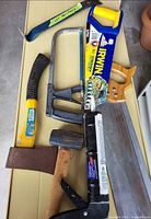 Overall view of eight hand tools including saws, hammers, pry bar, caulking gun, sanding block