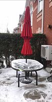 Full view of round glass patio table with red umbrella and base