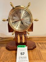 Front view of brass ship’s wheel table clock on wood stand