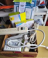 Overview of lot contents in box showing power strips, wall plate packs, cords