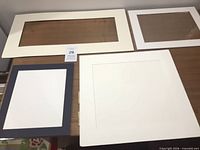 Four framing components laid out: two off-white mats, one dark charcoal mat, one clear frameless glass panel