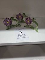 Set of three purple flower ceramic napkin rings on shelf