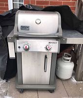 Full view of Weber Spirit stainless steel propane grill with cover and propane tank