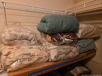 Stack of six comforters in plastic bags on shelf