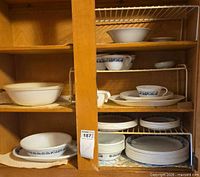 Cupboard shelf holding Corelle dinnerware stacks and serving pieces