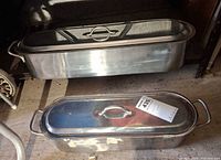 Two stainless steel fish poachers with lids, side view