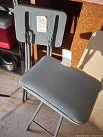 Front view of grey folding stool showing padded seat and backrest