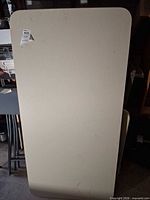 Full view of beige rectangular folding table standing upright