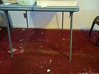 Square blue folding table with collapsible legs, contents on top not included