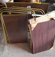 Stack of three gold-tone metal folding TV tray tables with brown laminate tops and boxed tilt-top table panel