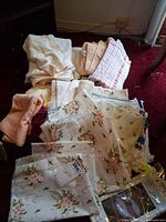 Pile of assorted towels, floral table linens, napkins and packaging on carpet