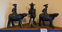 Group shot of two wooden water buffalo with riders, one wooden standing man, one ceramic mudman